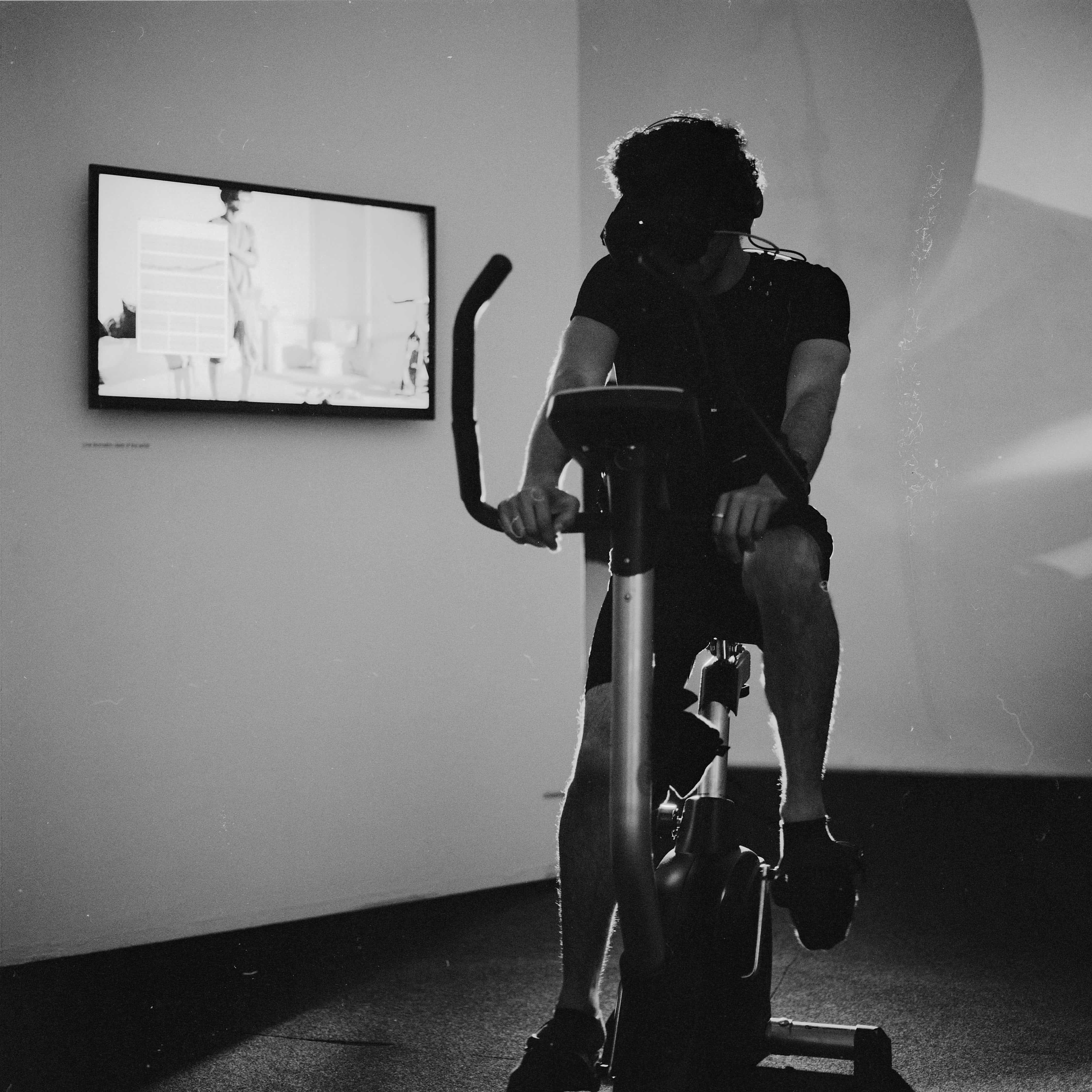 The artist with the VR headset on, on an exercise bike.